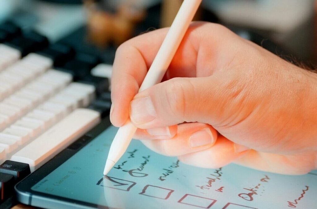 Hand füllt eine Checkliste auf einem Tablet aus zur Überprüfung von Projektzielen, Rollen, Planung, Risiken und Steuerung
